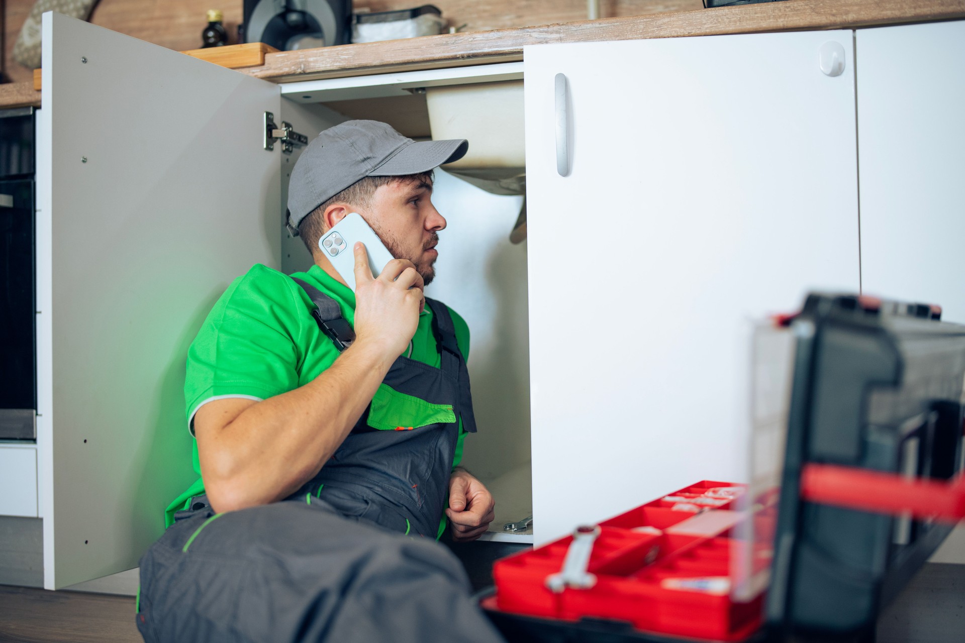 Plumber on a call while repairing a kitchen sink pipe.
